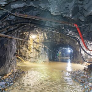 Dimly lit underground cave with flowing water and exposed pipes, showcasing rugged geology.